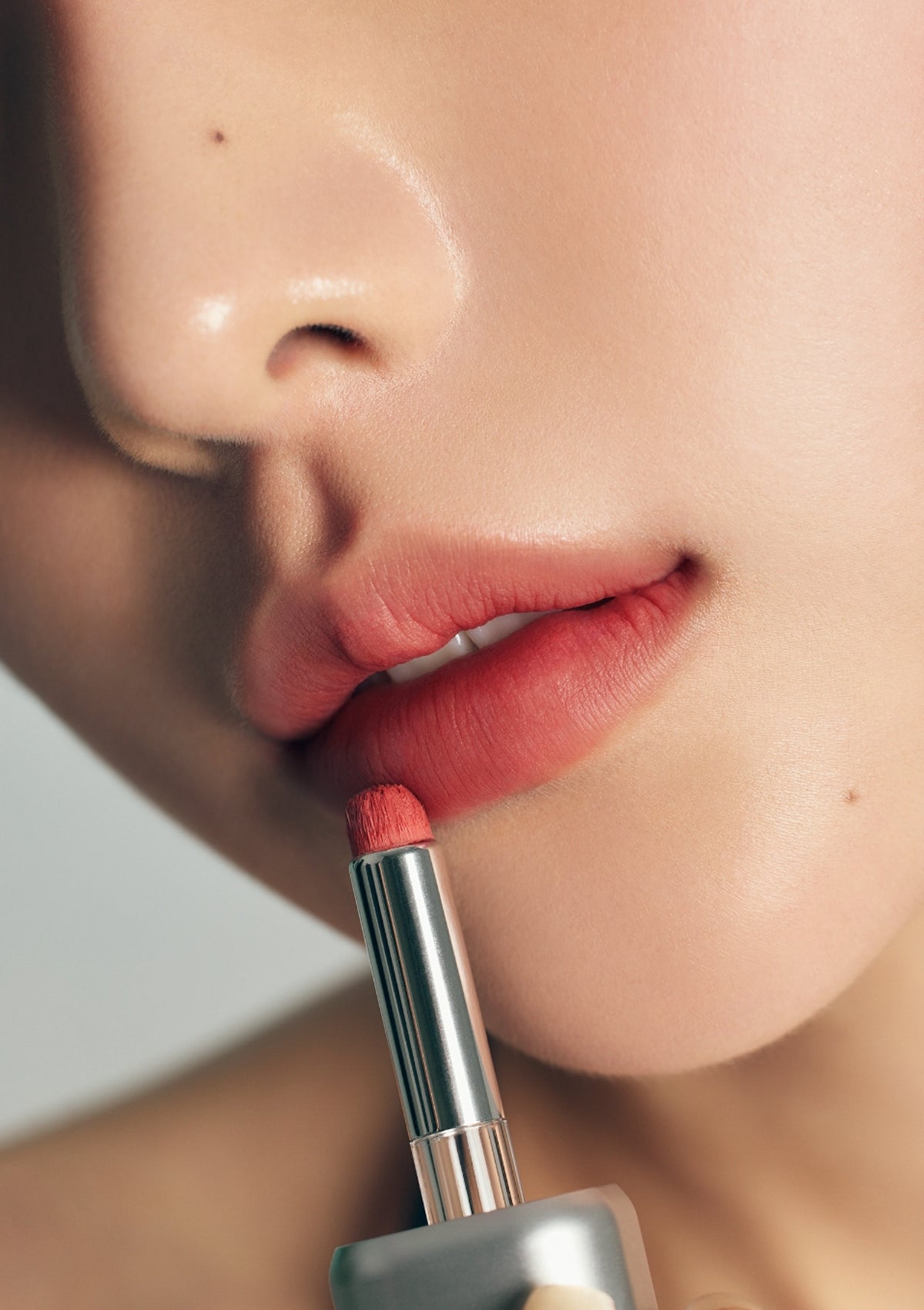 Close-up of a person applying pink lipstick to their lips.